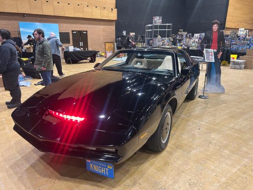 KITT, Knight Rider, at Comic Con Bournemouth Black sports car with a red light at the back, displayed at an event with people nearby.